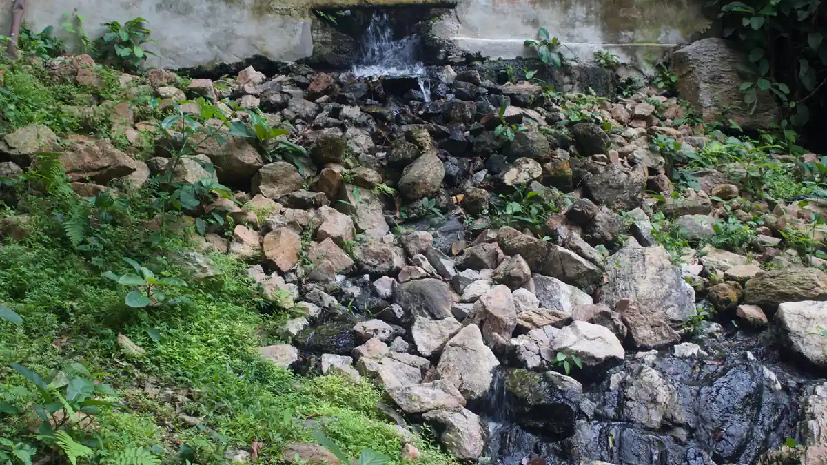 Water flowing over rocks beneath a concrete wall at Ikogosi Warm Spring, surrounded by green vegetation.